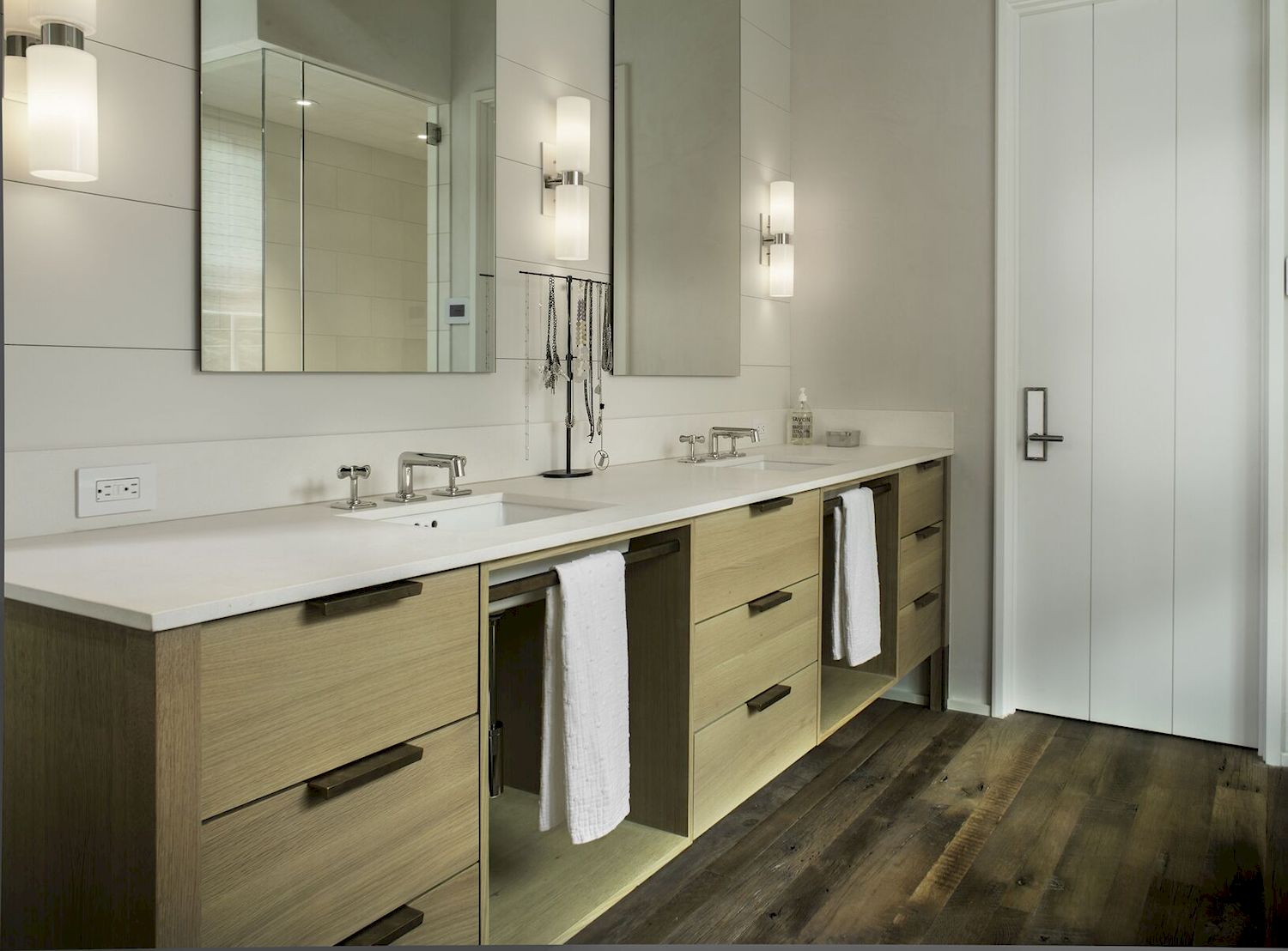 double sink vanity with three sets of sleek wooden drawers. Between the sets of drawers, there is open storage space and towel bars mounted for hand towels. 